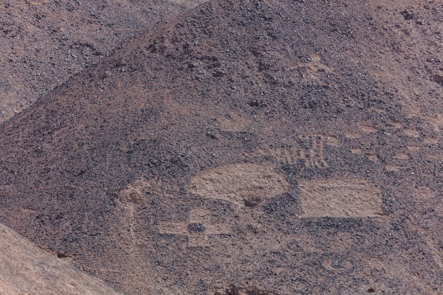Geometric and animal geoglyphs covering a brown hillside at Cerros Pintados