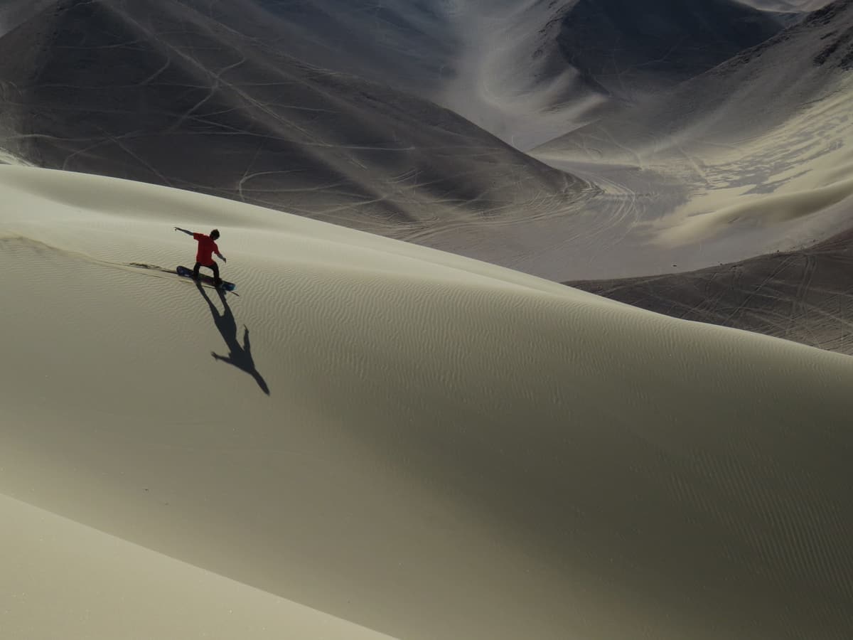 A sandboarder riding down a huge dune near Iquique